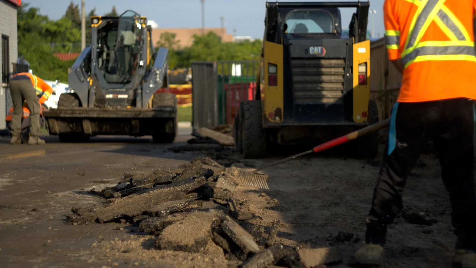 Crew members and skid-steer loaders remove broken asphalt at the Kal Tire project.