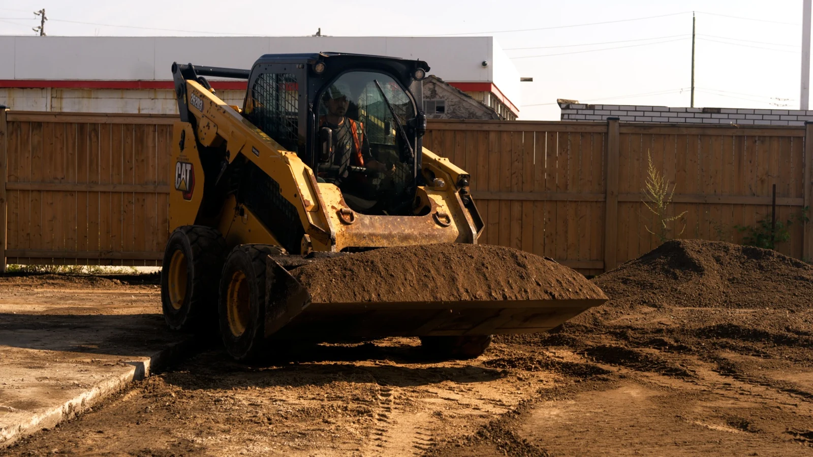 A skid-steer operator moves material during site preparation at the Kal Tire project.