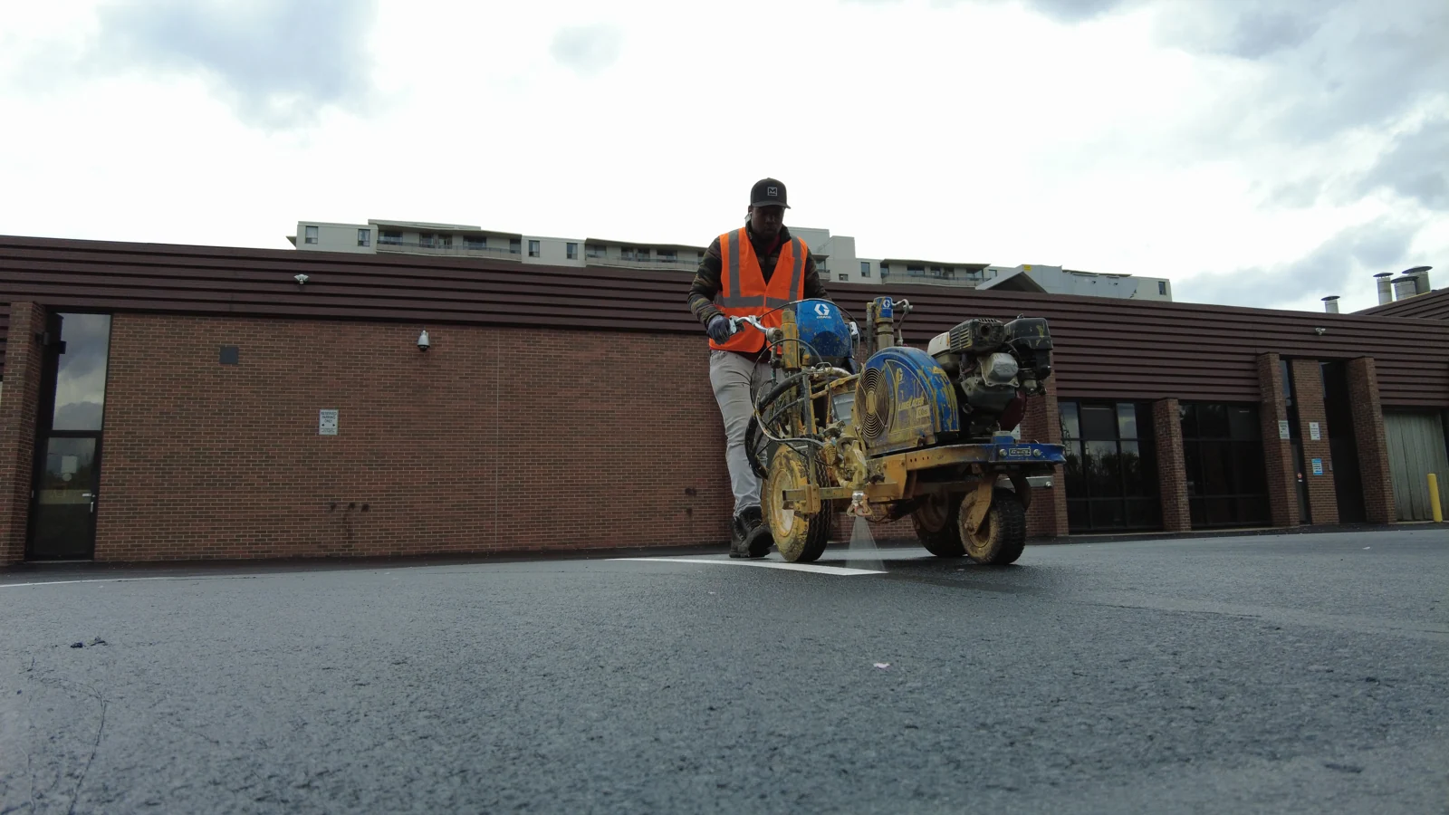 A line painting operator applies a fresh white parking lot marking.